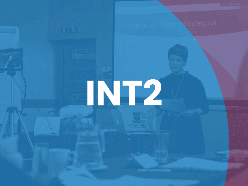 A woman stands and presents in a conference room with a projected slide behind her; the text "INT2" is overlaid on the image.