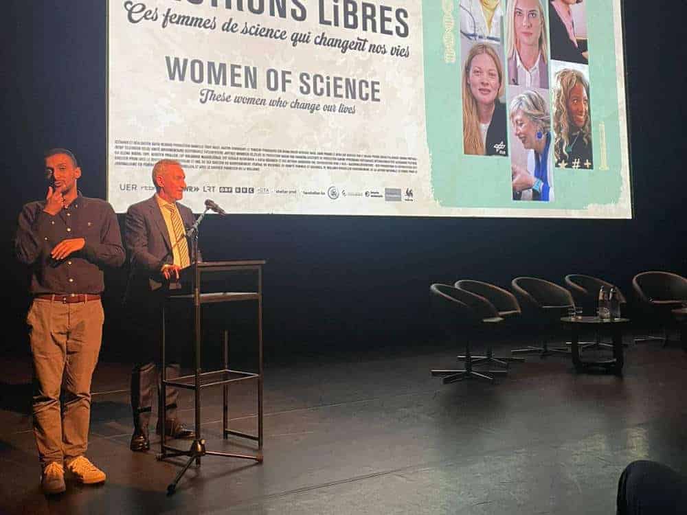 A stage with speakers and a large screen displaying the "Women of Science" banner, showcasing female scientists.
